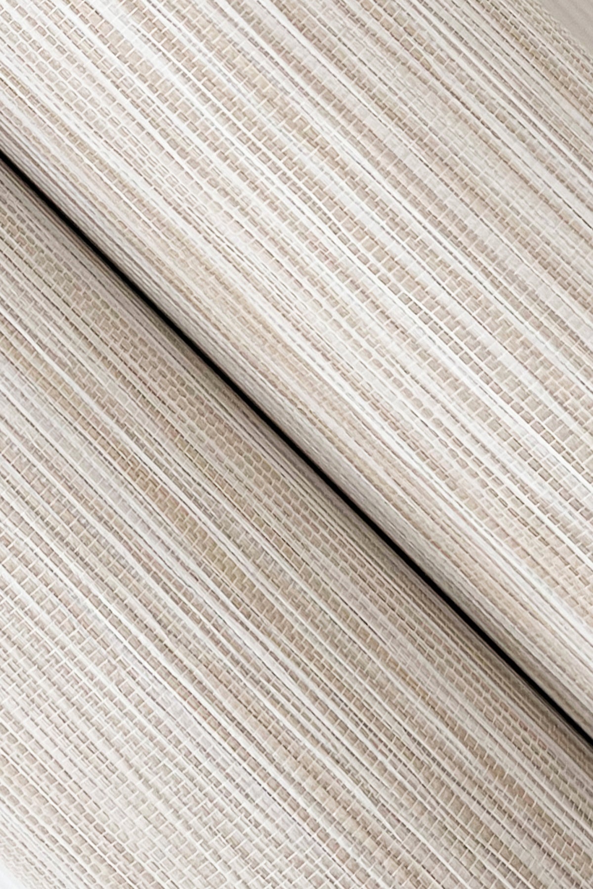 Beige striped grasscloth wallpaper close-up showing a woven texture with a ribbed appearance and diagonal seam.