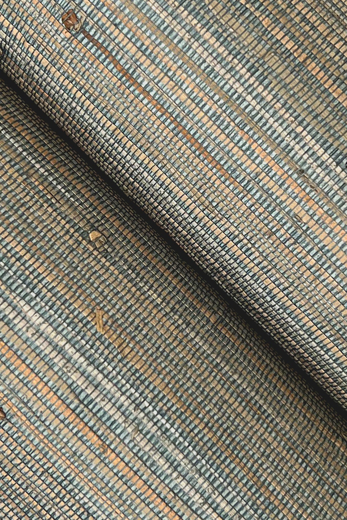 Close-up of grasscloth wallpaper texture with blue, tan & gray threads in a small rectangular grid; rolled edge.