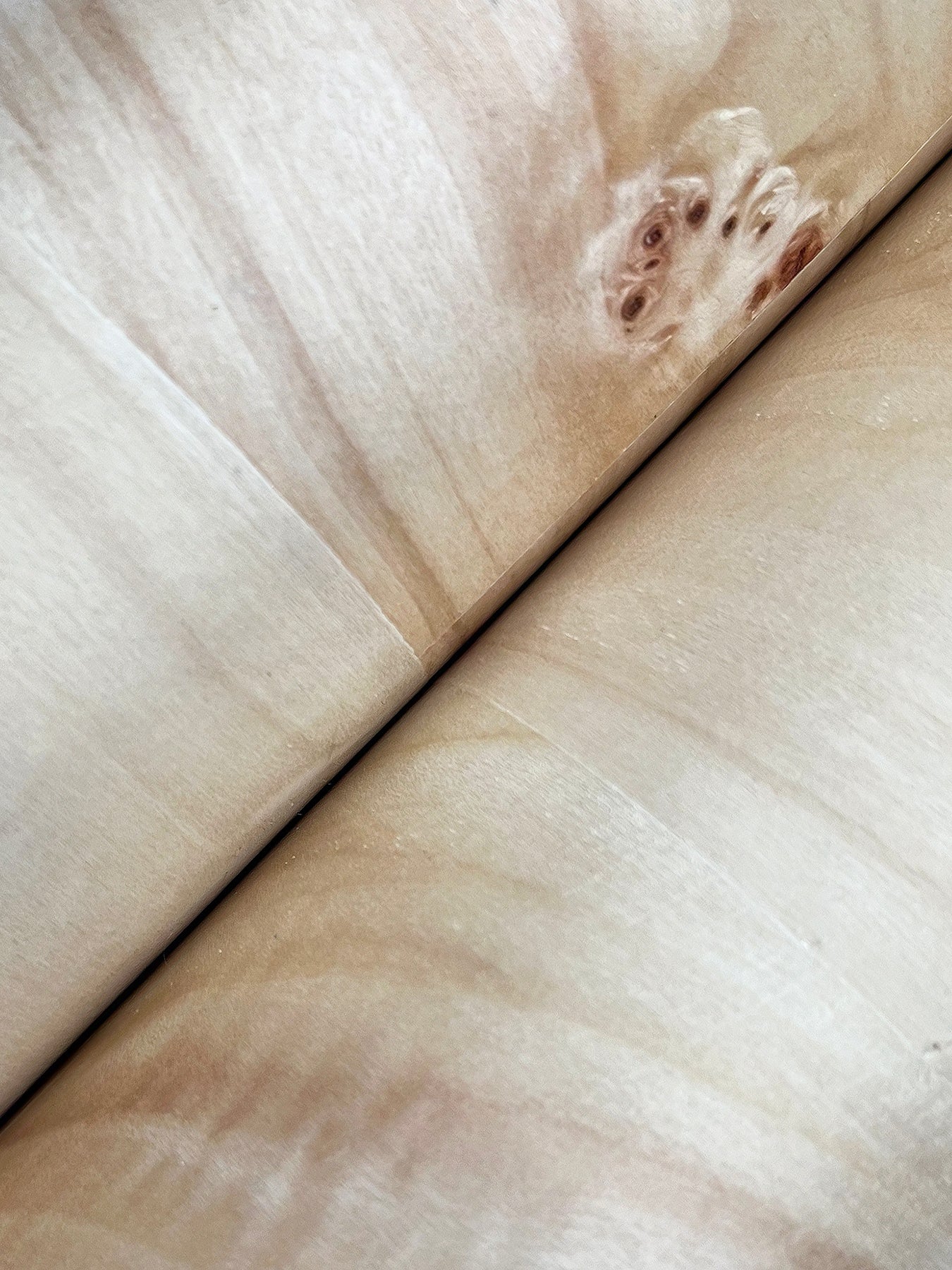 Close-up of pale beige wood grain with a diagonal seam, showcasing natural veneer texture.