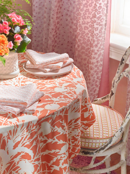 Round dining table with peach-orange wildflower fabric as a table covering, matching napkins, white plates & a vase of flowers.