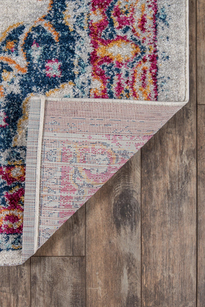 Vibrant patterned area rug with blue, pink and yellow motifs; plush pile, corner lifted to show woven underside on floor.