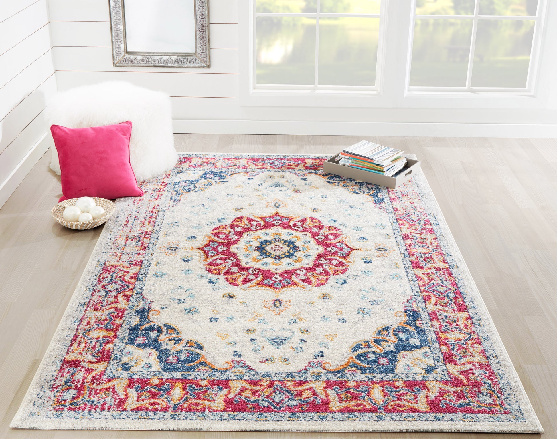 Oriental-style area rug with ivory field, rich red and blue border and central medallion in a bright cozy living room.