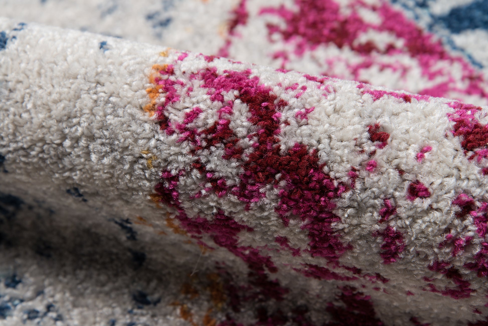 Close-up of a plush area rug with white base and bright magenta pink pattern, with hints of orange and blue.