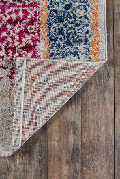 Vibrant patterned area rug with pink magenta, blue ornate field, orange border, folded corner reveals beige backing on wood floor.