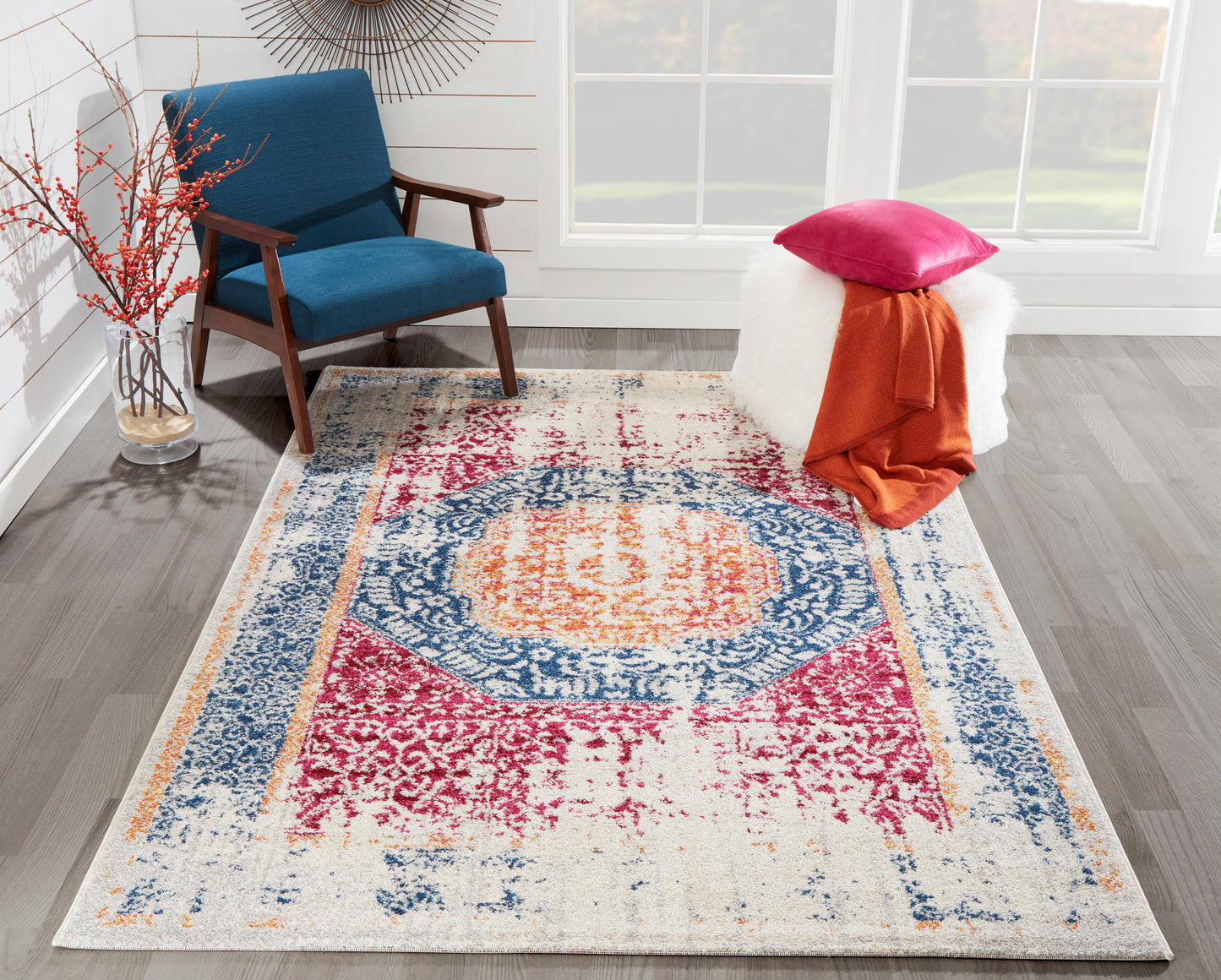 Vibrant distressed area rug with blue border, pink accents, and orange center, laid in a living room beside a blue chair.