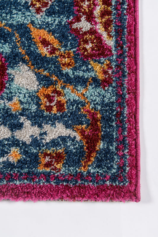 Close-up of a plush, vibrant patterned rug with blue field, magenta border and pink trim; floral motifs in teal, orange and gold.