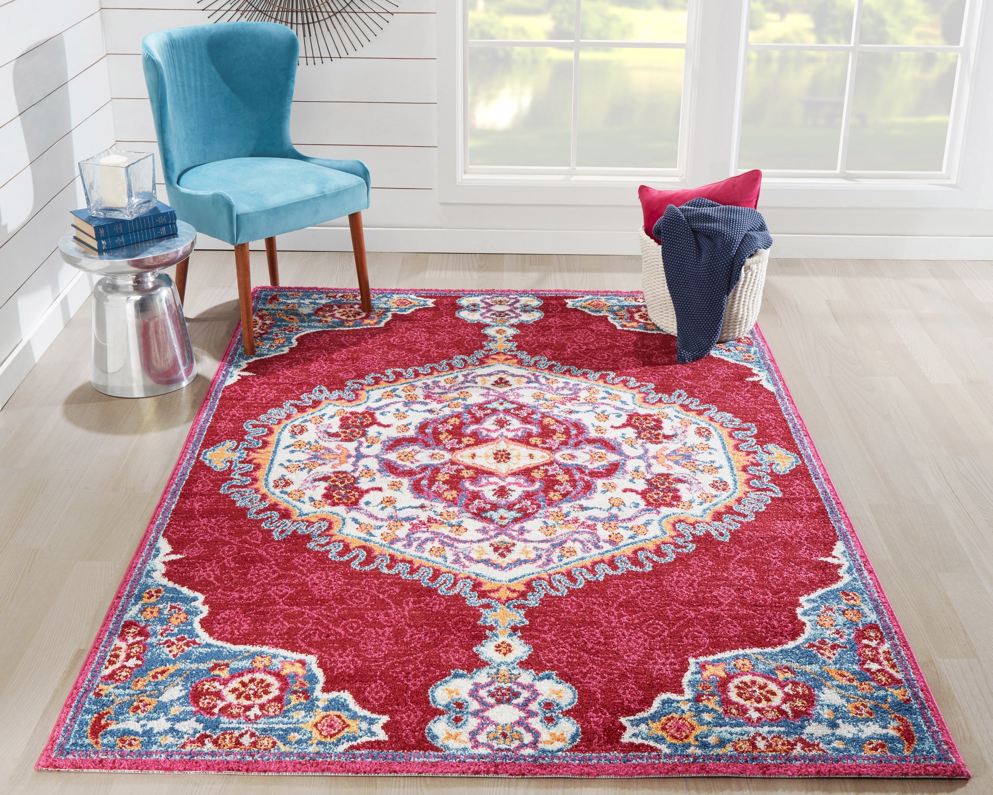 Magenta oriental rug with turquoise and ivory medallion, ornate border, in a bright room with a blue velvet chair.