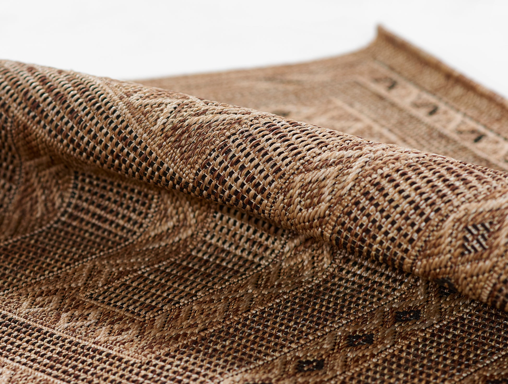 Natural brown woven rug in a rolled corner, close-up of a coarse lattice pattern and rustic texture.