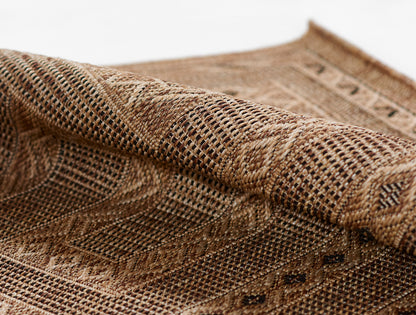Close-up of a natural brown woven rug in jute with geometric pattern and chunky textured weave.