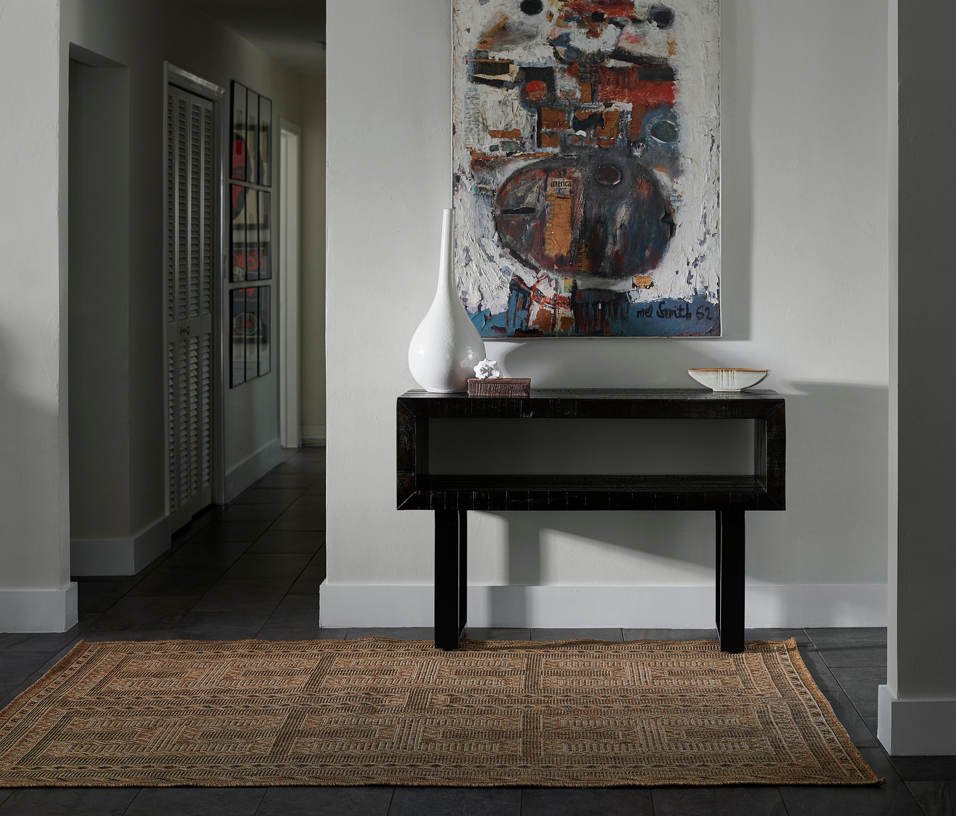 Natural fiber rug beneath an abstract painting & a black lacquered console table with a white ceramic vase & bowl.