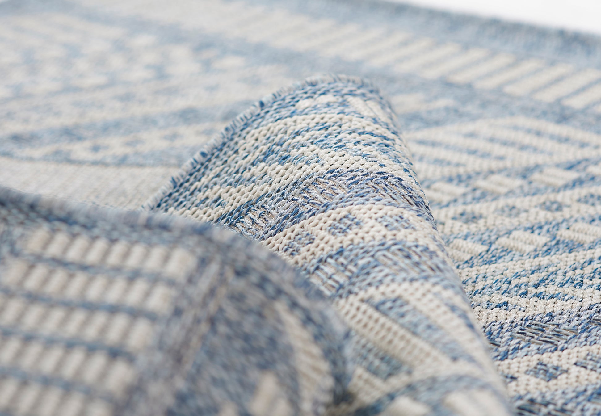 Close-up of a blue and ivory woven rug with geometric pattern and textured fibers.