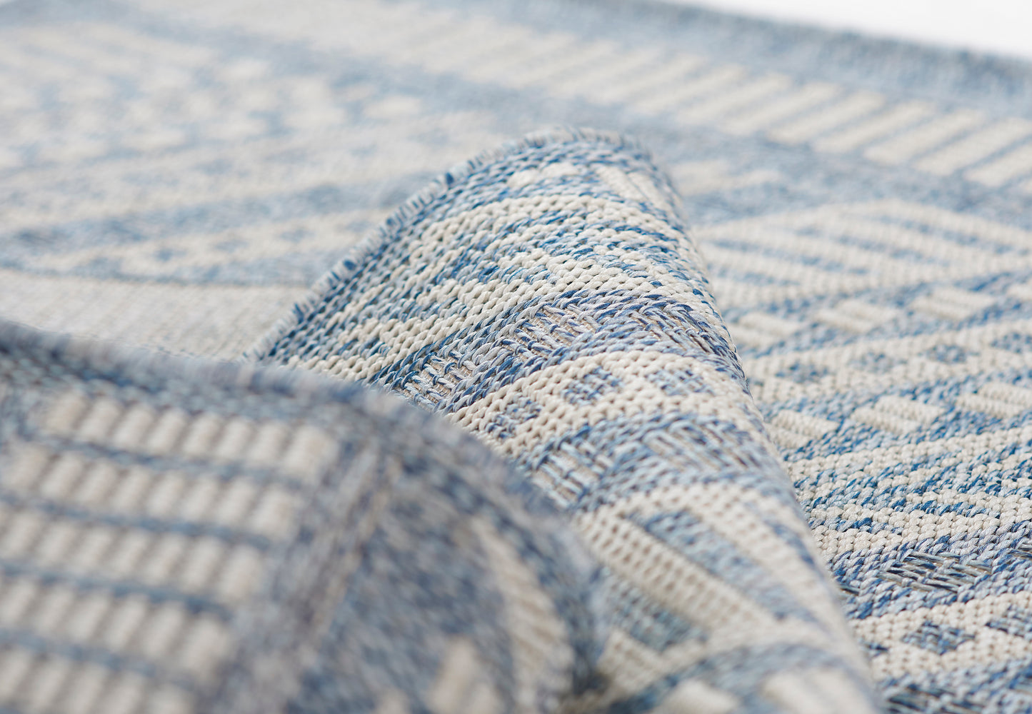 Close-up of blue and ivory woven rug with geometric diamond pattern and folded corner.