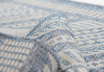 Close-up of blue and ivory woven rug with geometric diamond pattern and folded corner.