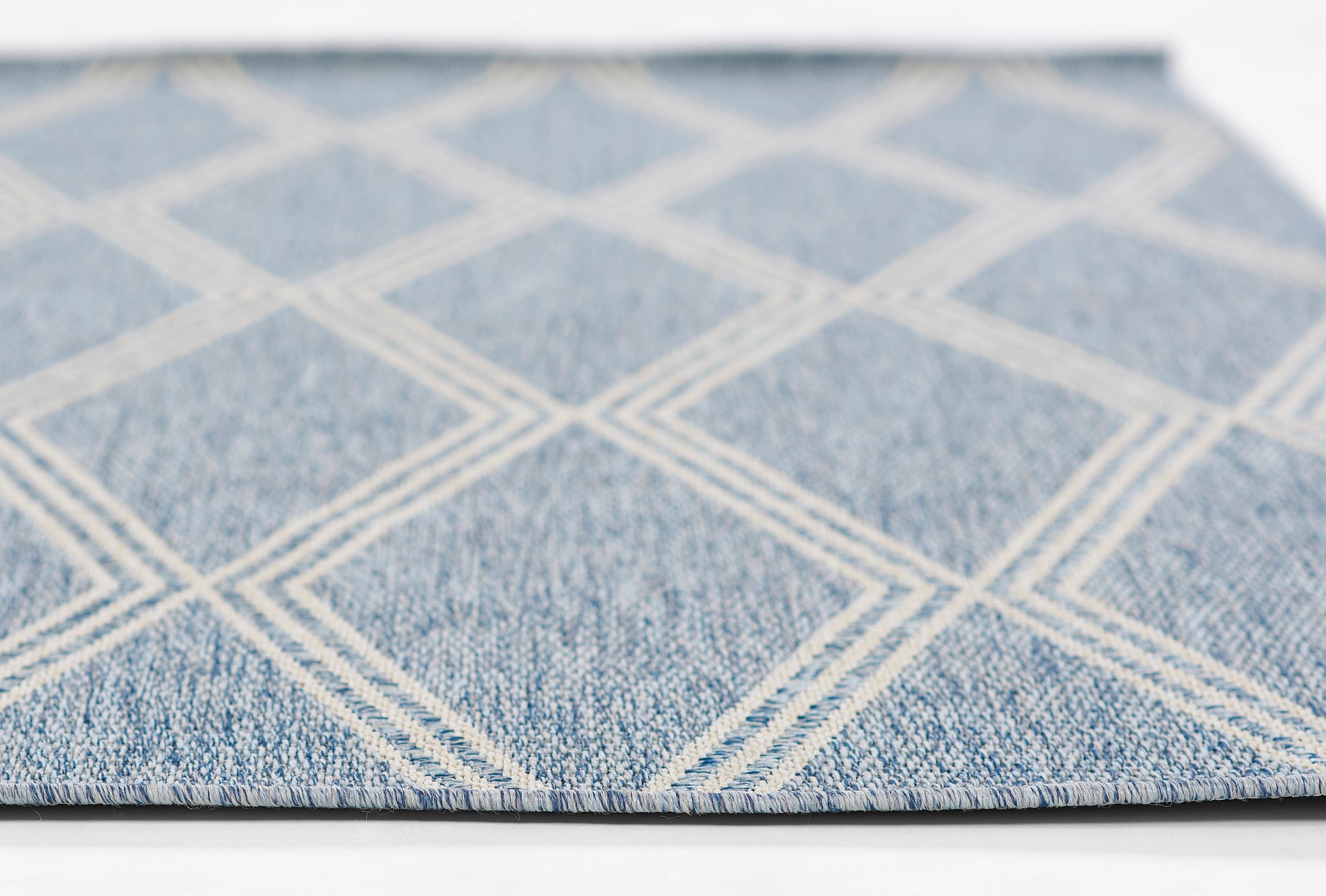 Blue rug with white diamond lattice pattern, denim-like texture, flat-weave style, close-up view