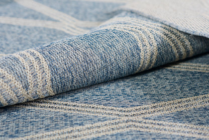 Close-up of blue woven rug with striped off-white pattern, denim-like texture and rolled edge.