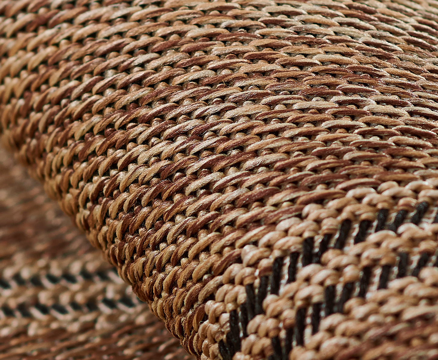 Close-up of a natural straw woven rug runner in tan-brown tones with a black stripe, showing textured rustic craftsmanship.
