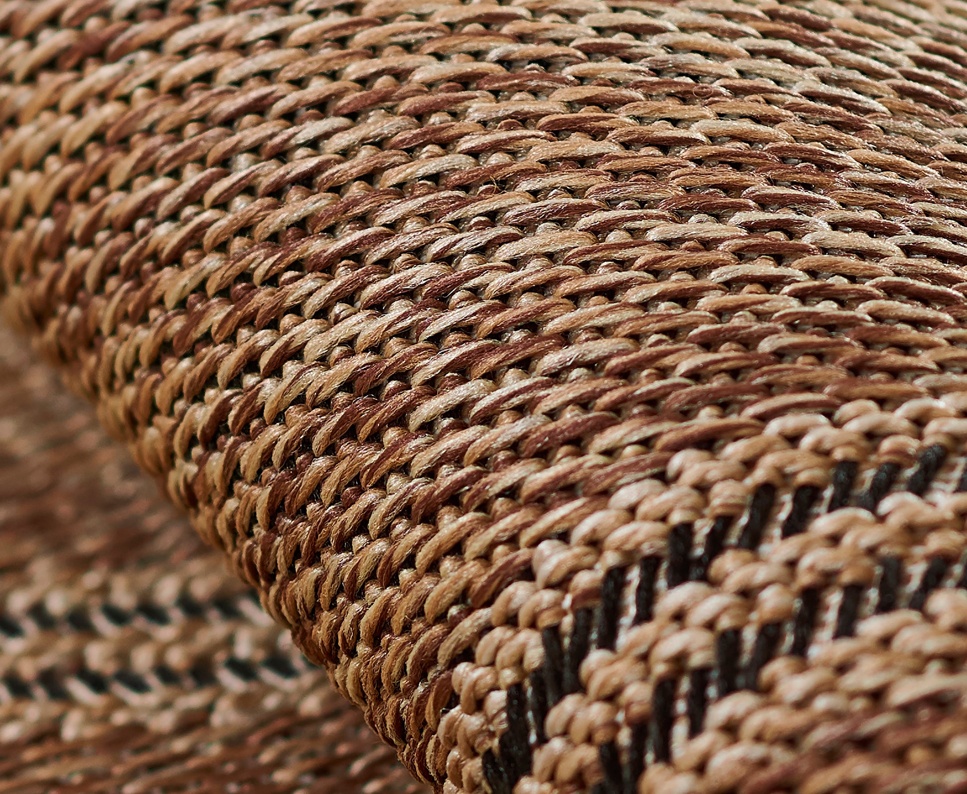 Close-up of a natural straw woven rug runner in tan-brown tones with a black stripe, showing textured rustic craftsmanship.