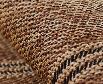 Close-up of a natural straw woven rug runner in tan-brown tones with a black stripe, showing textured rustic craftsmanship.