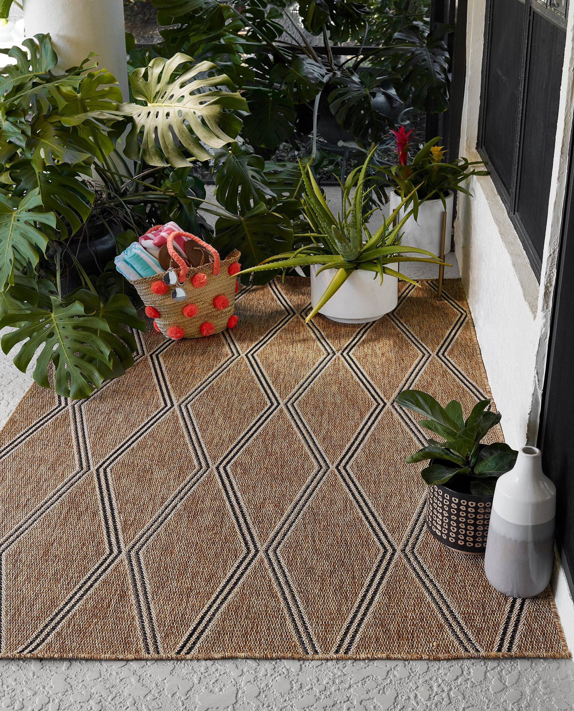 Natural jute outdoor runner rug with a black diamond geometric pattern on a porch, surrounded by potted tropical plants, 3' x 8'.
