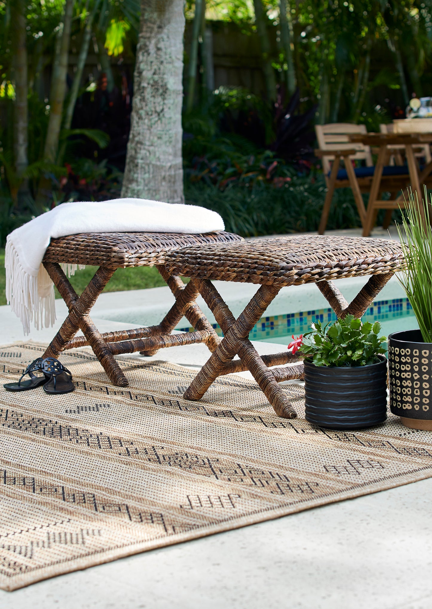 Beige patterned outdoor rug with a natural woven texture, featuring a white throw on it beside a pool.