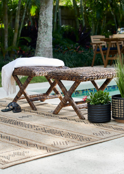 Beige patterned outdoor rug with a natural woven texture, featuring a white throw on it beside a pool.