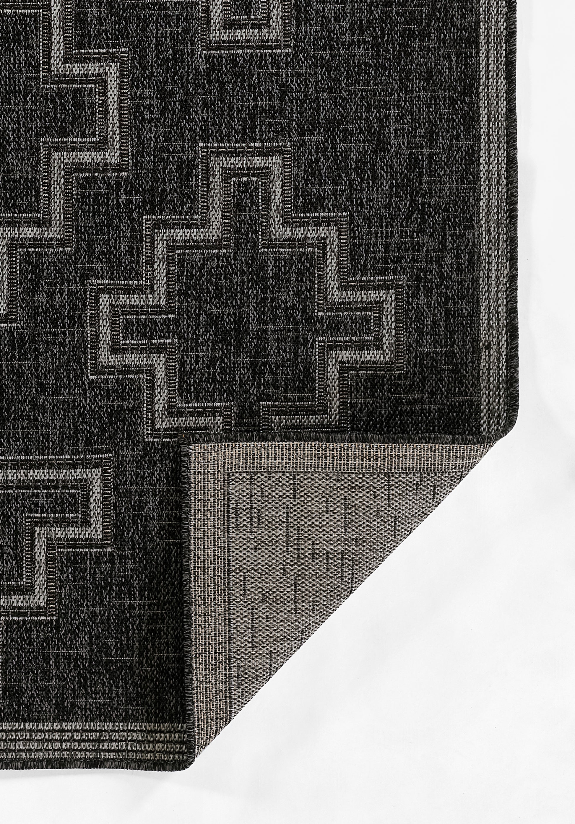 Black geometric area rug with light gray cross motifs; woven texture, folded corner reveals lighter underside.