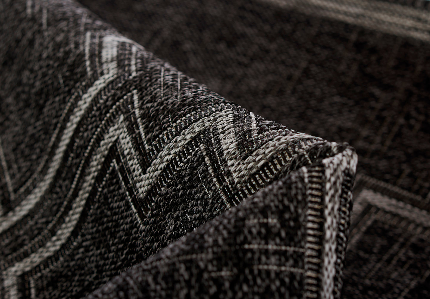Close-up of a dark charcoal woven rug with a light gray chevron zigzag pattern and a folded edge.