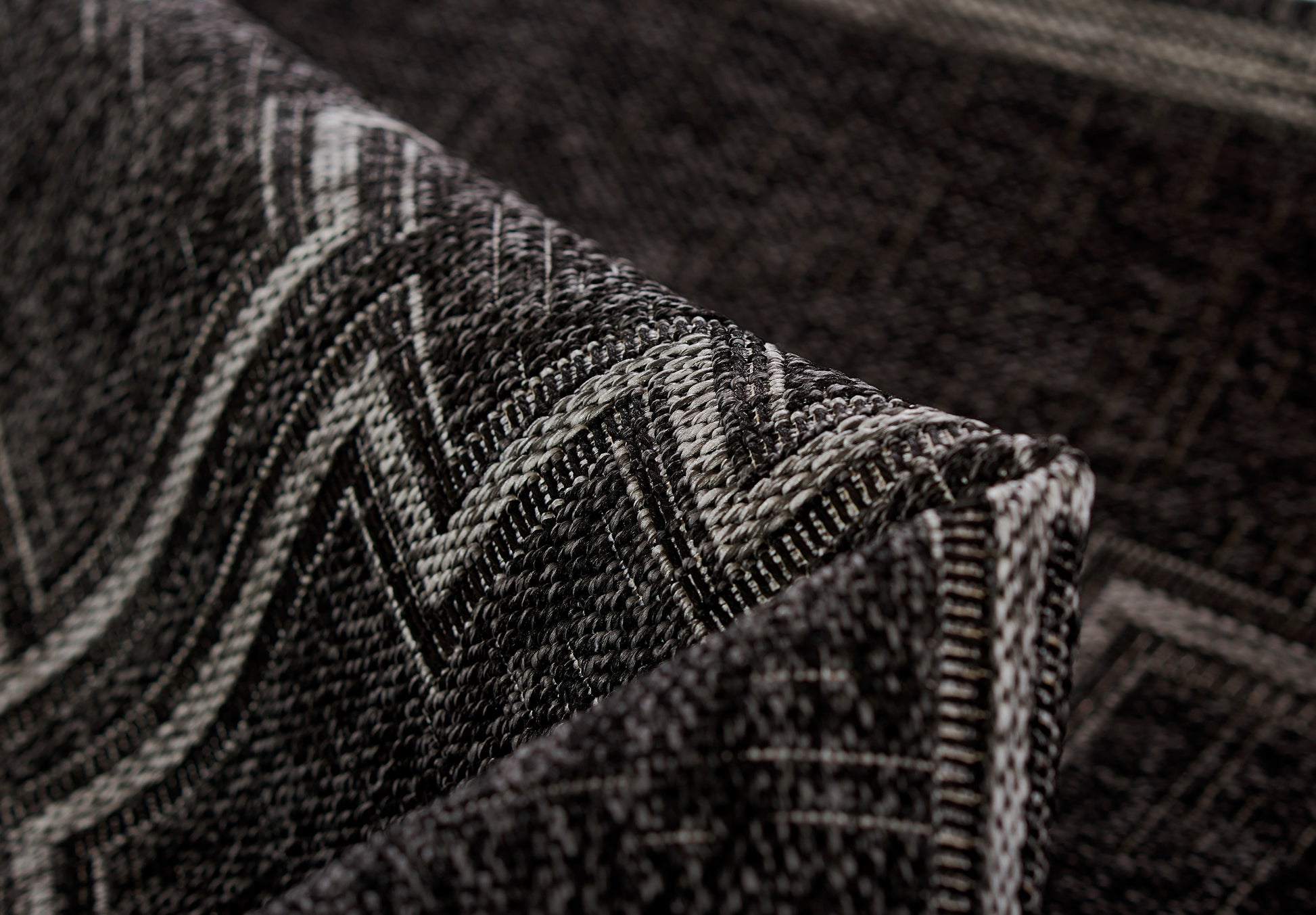 Close-up of a dark charcoal woven rug with a light gray chevron zigzag pattern and a folded edge.