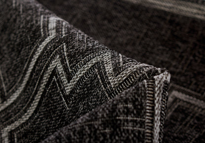 Close-up of a dark charcoal woven rug with a light gray chevron zigzag pattern and a folded edge.