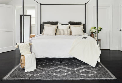 White four-poster bed with black metal frame, cream bedding, beige and faux-fur pillows, white throw, gray geometric rug.