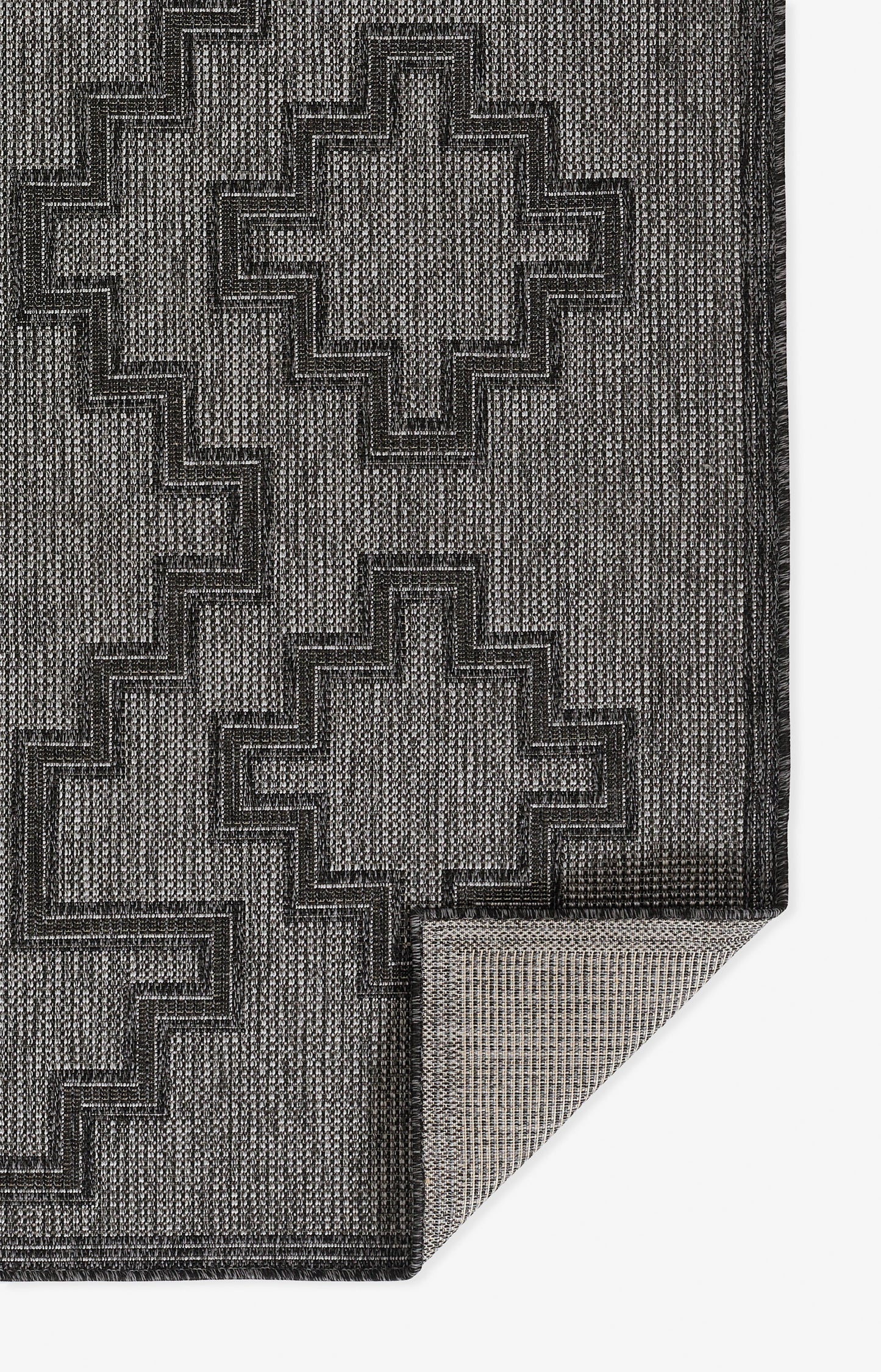 Charcoal and grey woven rug with stepped cross motifs; textured geometric pattern, folded corner reveals lighter underside