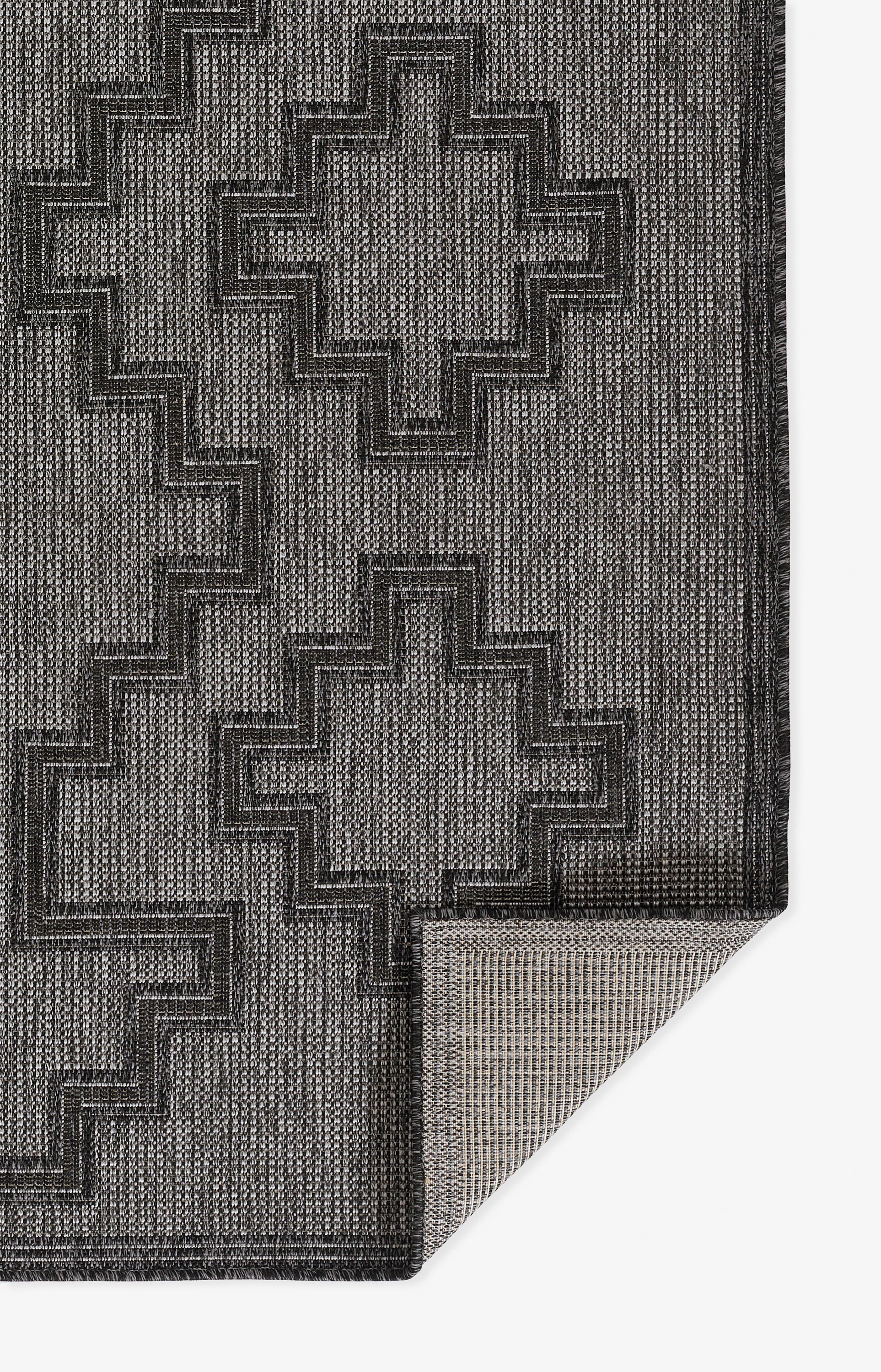 Gray and charcoal black geometric area rug with stepped cross motifs; woven texture, folded corner shows backing.