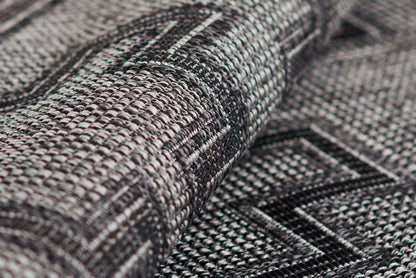 Close-up of a rolled grey & black woven rug with geometric pattern and chunky textured yarns.