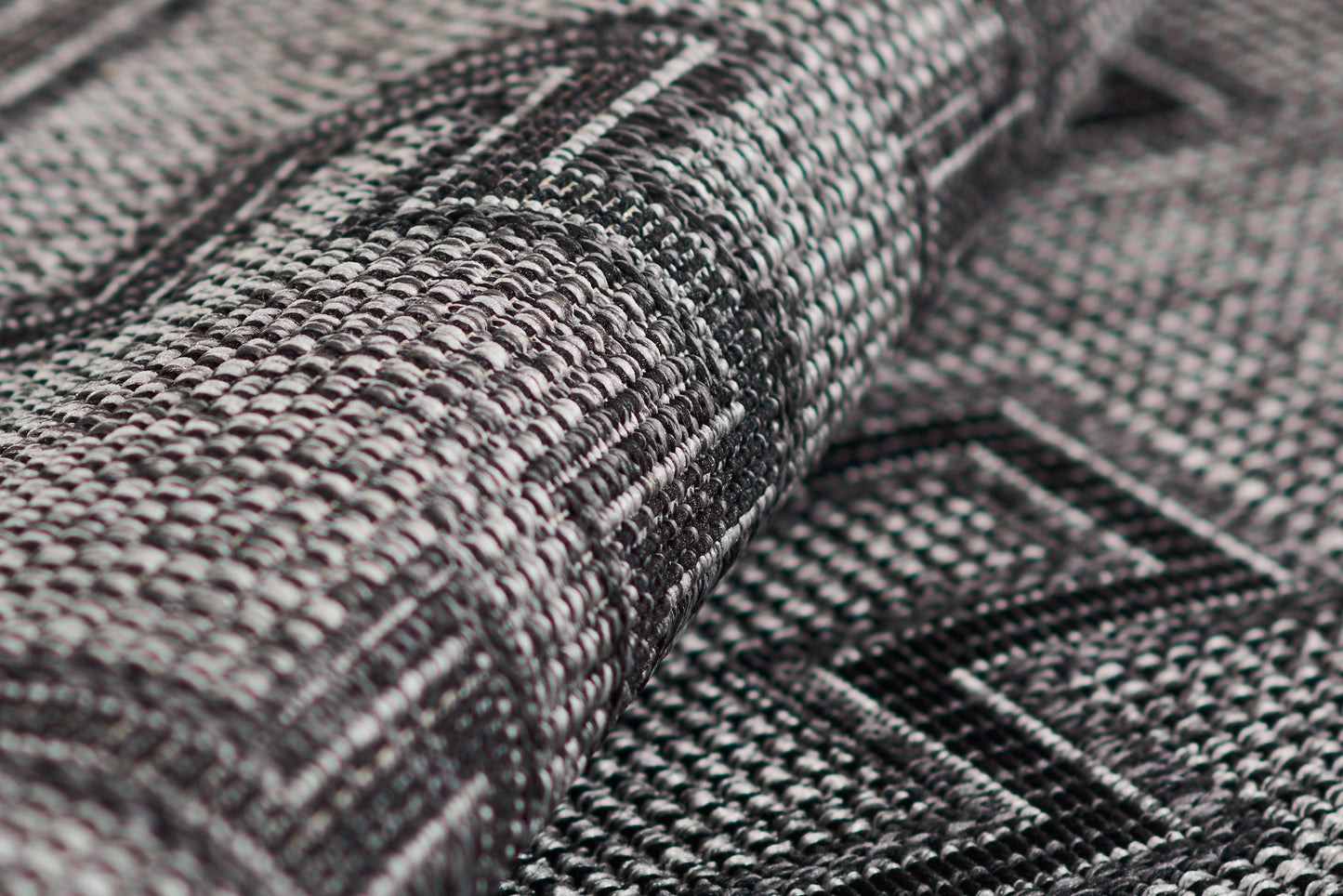 Rolled gray and black woven rug with tight geometric pattern and textured weave.