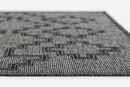 Gray and black geometric rug with interlocking rectangular maze pattern and subtle striped texture.