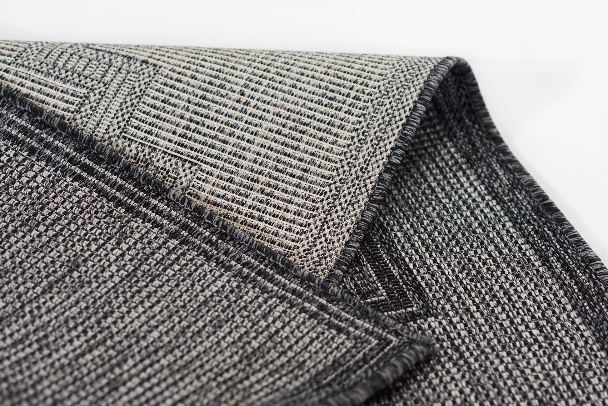 Close-up of gray and charcoal woven fabric rug with plaid and grid patterns, rolled edges.