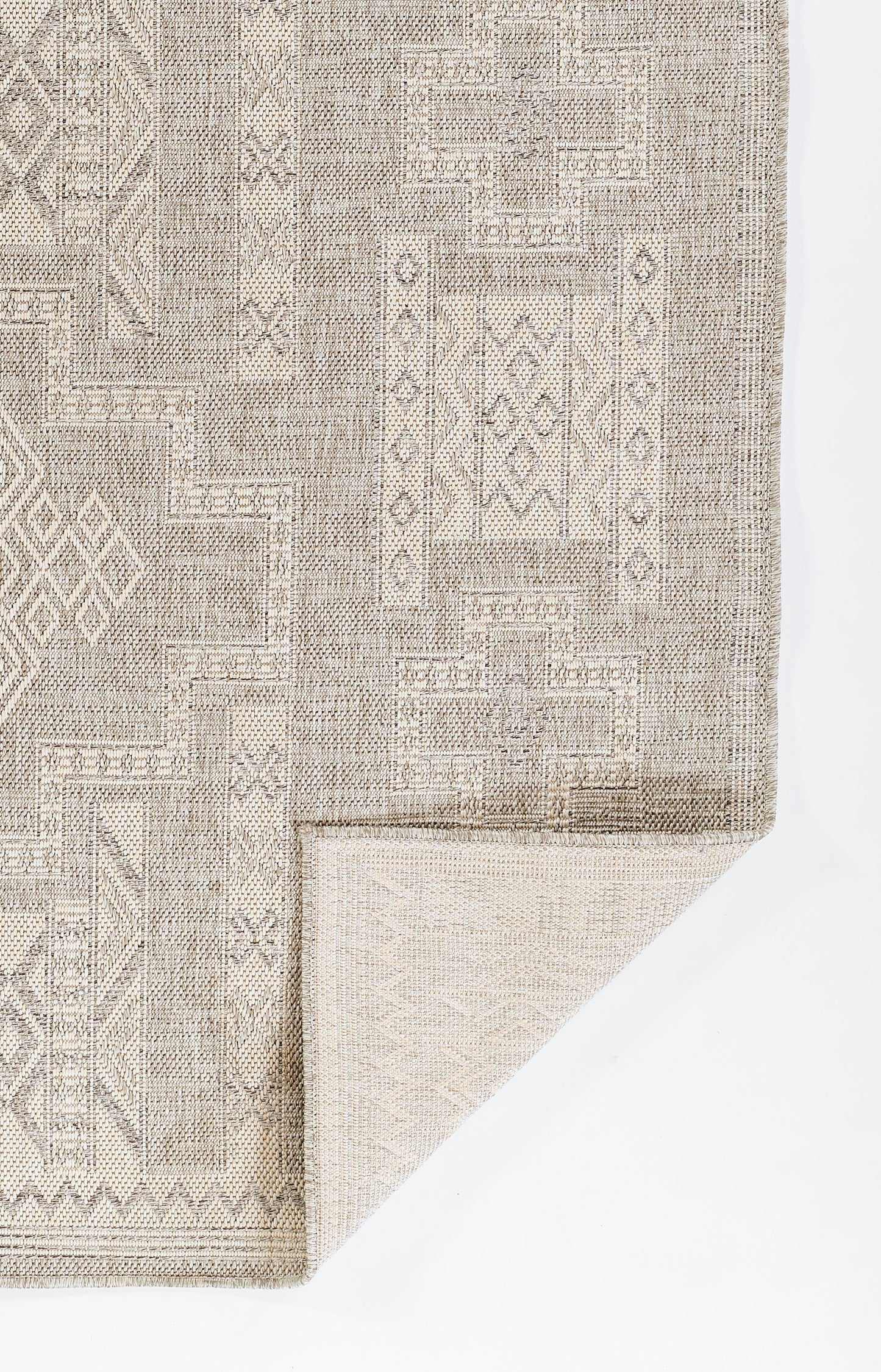 Beige-gray geometric patchwork area rug with woven texture and bordered edges; folded corner reveals lighter underside.