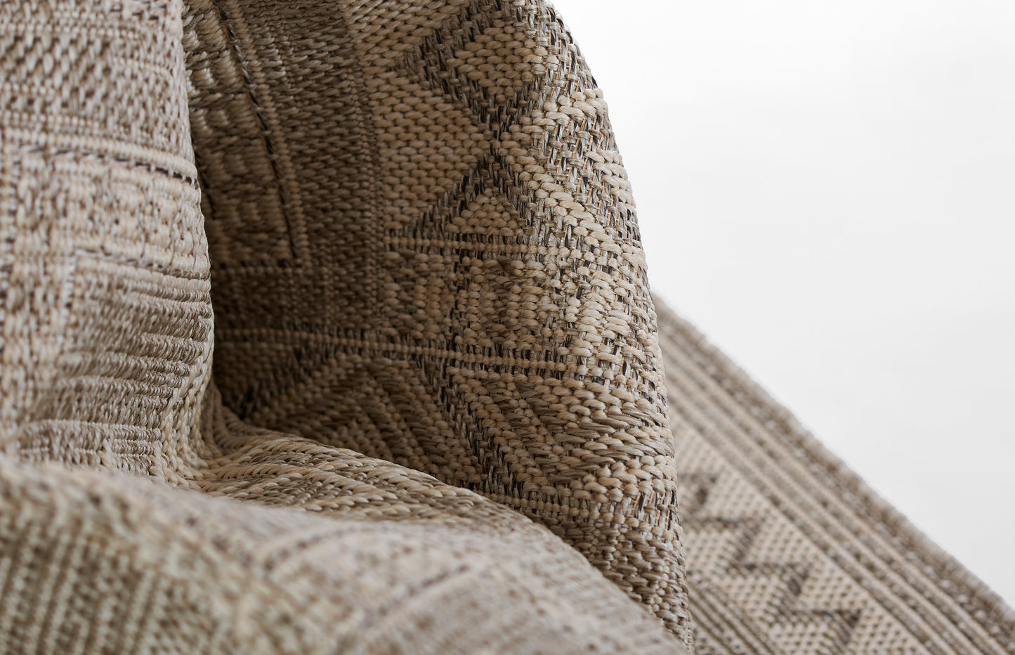 Close-up of a gray beige woven rug with a diamond geometric pattern and textured jute fibers.