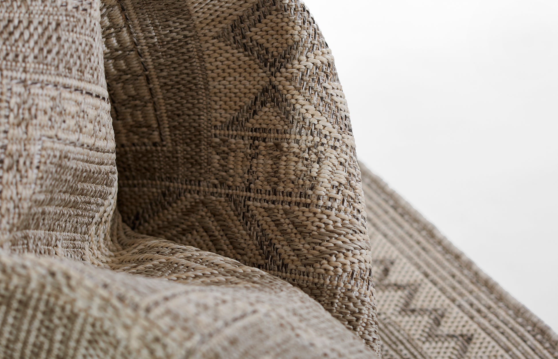 Close-up of a gray beige woven rug with a diamond geometric pattern and textured jute fibers.