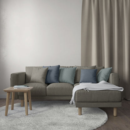 Taupe fabric sectional sofa with blue-gray cushions, round wooden coffee table, and a white throw in a neutral living room.