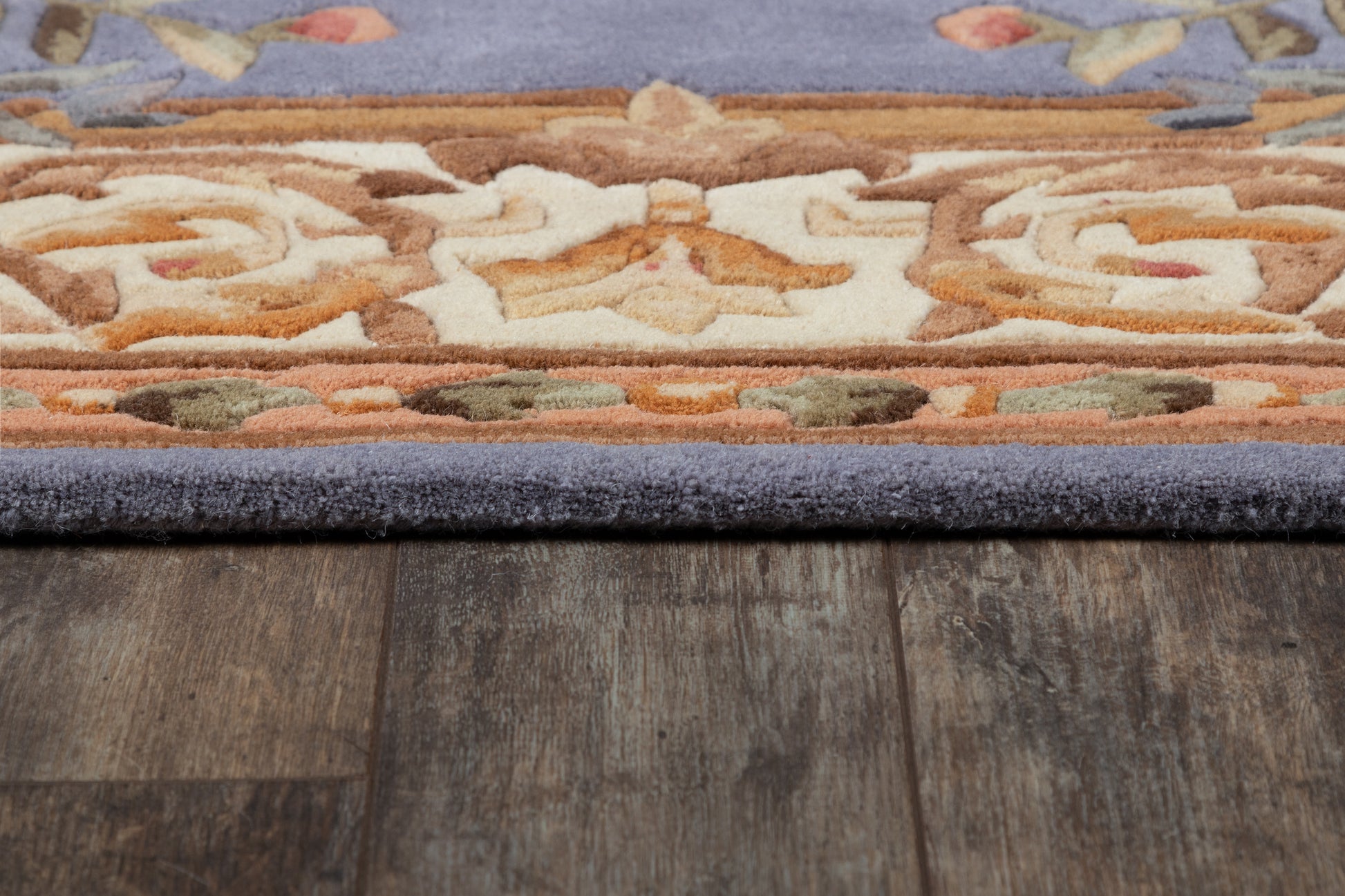 Blue-edged oriental-style rug with cream, orange, brown and green motifs on dark wood floor.