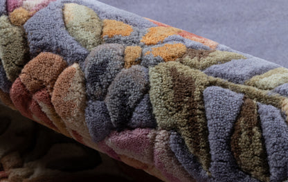 Colorful tufted rug with a geometric diamond pattern in blues, purples, greens, browns and orange, rolled up.