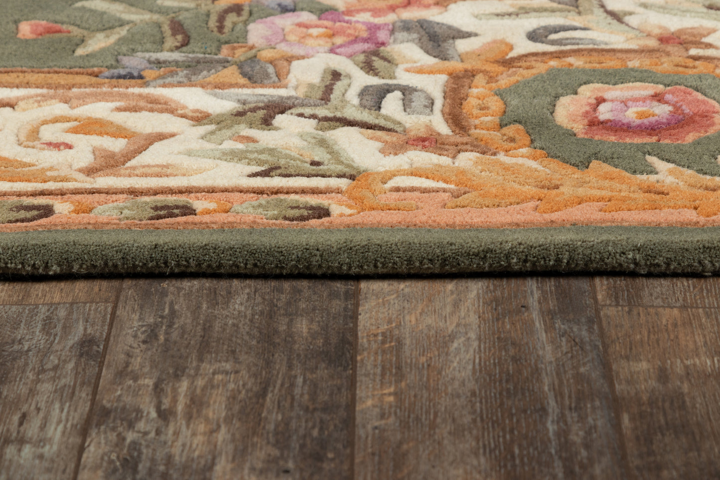 Close-up of ornate green-bordered runner rug on dark wood floor; warm orange, pink and cream floral pattern with plush pile.