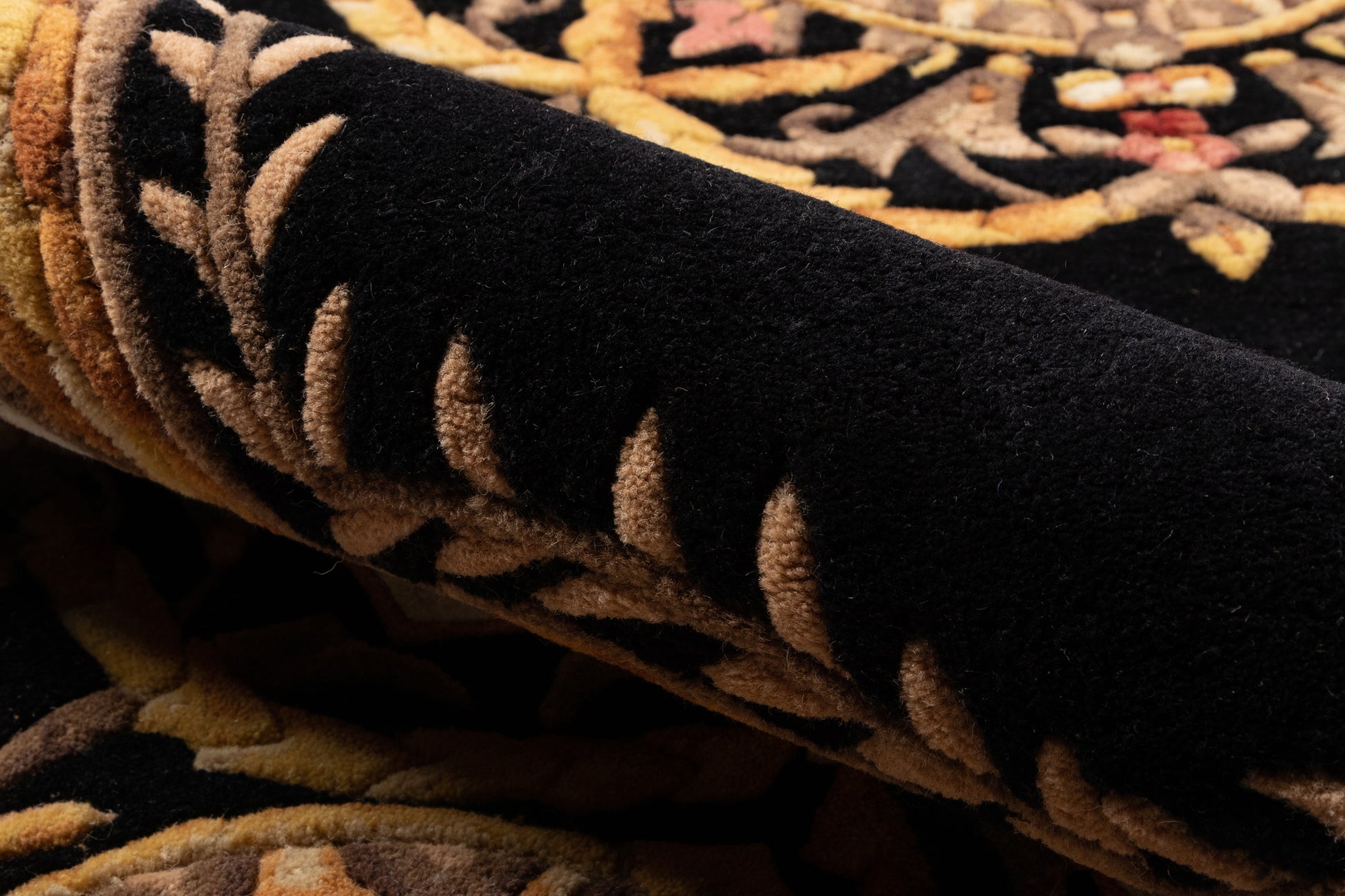 Rolled black oriental rug with tan and beige floral motif, plush pile.