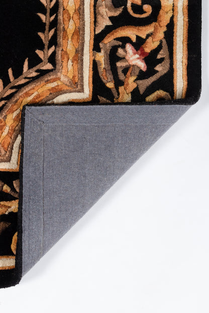 Ornate oriental rug in black, gold and rust with a border motif; blue-gray fabric backing folded over.