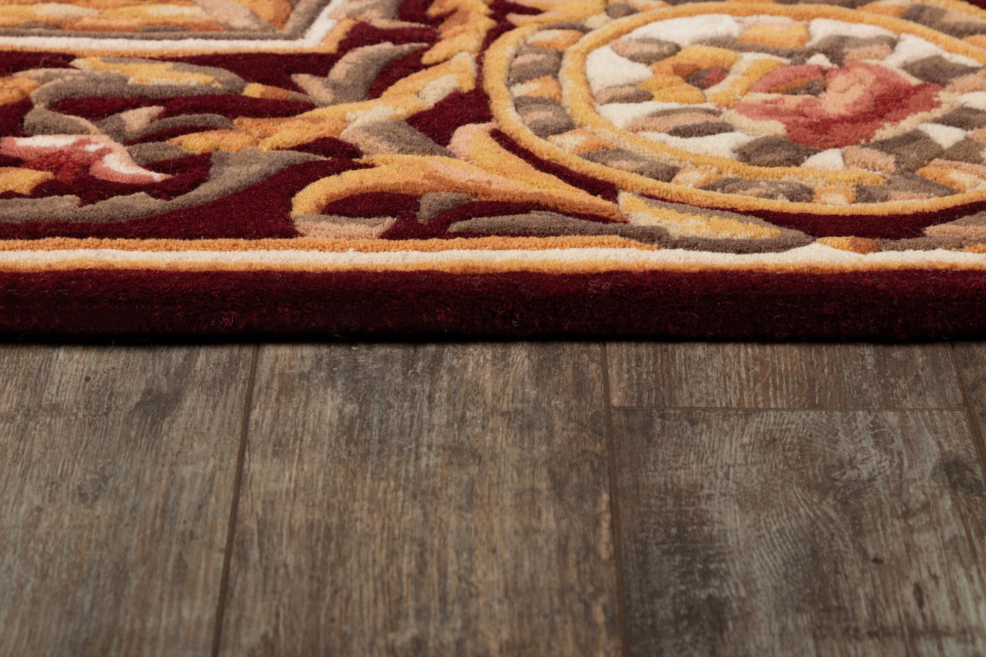 Ornate red, orange and beige rug edge with gray accents atop weathered wood floor.