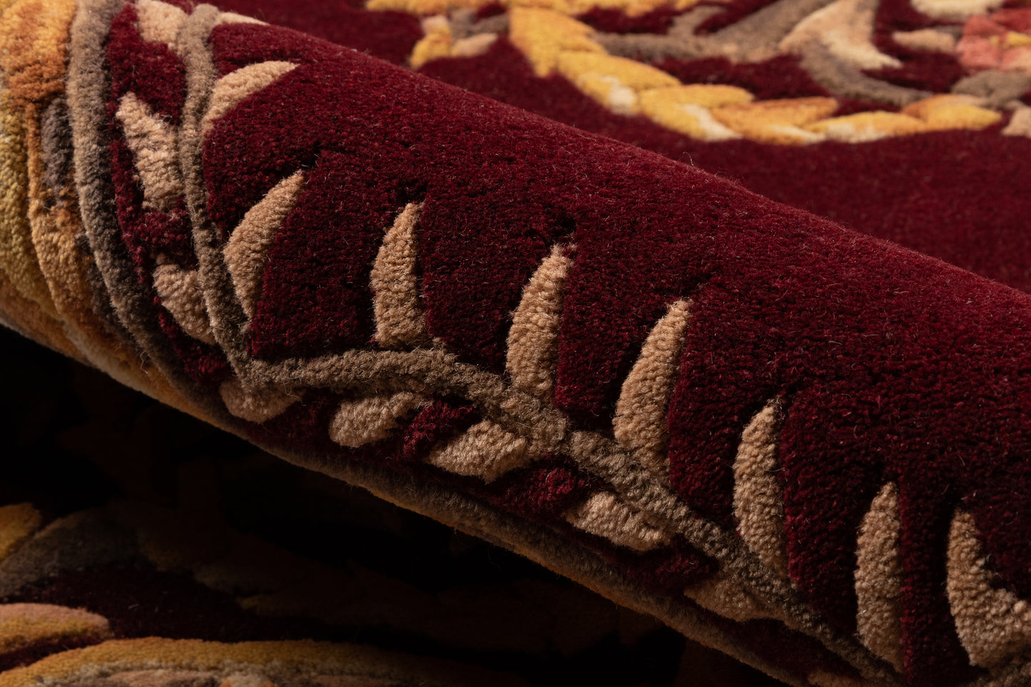 Close-up of burgundy plush rug with tan leaf motif and mustard border, rolled.