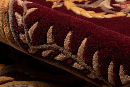 Rolled burgundy wool rug with beige leaf border in a Persian-inspired pattern.