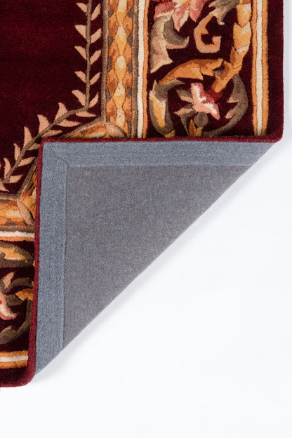 Decorative burgundy oriental rug with gold and tan floral border; folded corner reveals blue-gray underside.