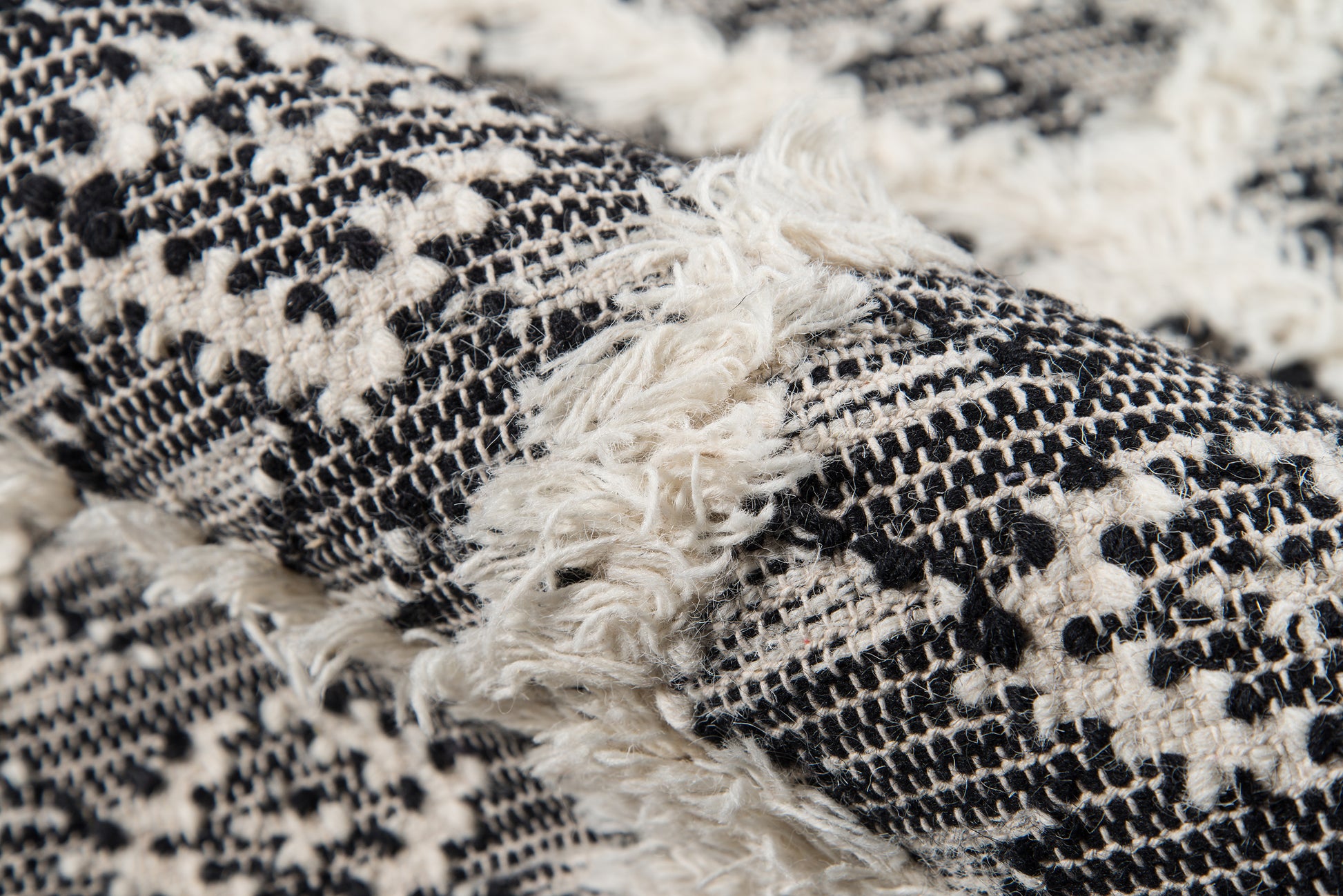 Black and white woven rug with geometric pattern and fluffy white fringe.